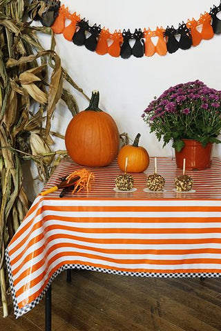 Freckled Sage oilcloth tablecloth stripe orange with black gingham trim with fall halloween display apples flowers pumpkins and corn on table